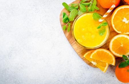 One glass of freshly pressed orange juice with a straw and mint leaves on a wooden board and light stone background. Top view, horizontal image, copy spaceの写真素材