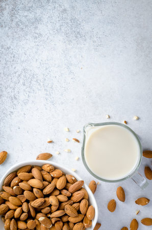 Almond milk in a milk pitcher with almond nuts on a light stone background. Top view, vertical image, copy spaceの写真素材