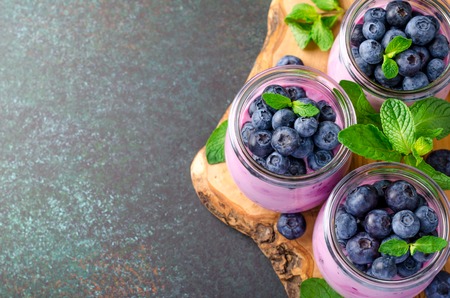 Three glasses of blueberry yogurt with blueberries on a wooden board and dark stone background. High angle view, copy space, horizontal imageの写真素材