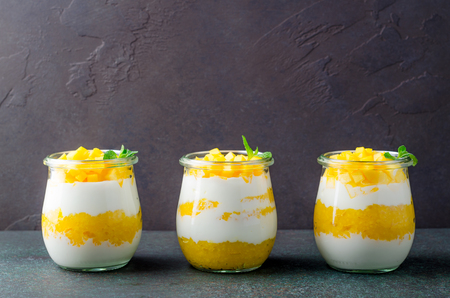 Three glass jars with greek yogurt and mango in a row on a dark table. Copy space, horizontal image, front viewの写真素材