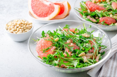 Grapefruit and arugula salad with pine nuts in glass bowls on a light gray stone concrete table. Horizontal image, high angle viewの写真素材