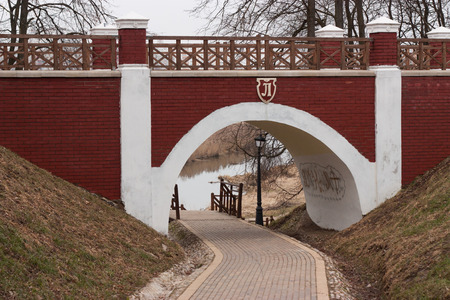 Arch brick footbridge with wooden railing in the city park and footpath beneathの写真素材