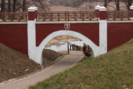 Arch brick footbridge with wooden railing in the city park and footpath beneathの写真素材
