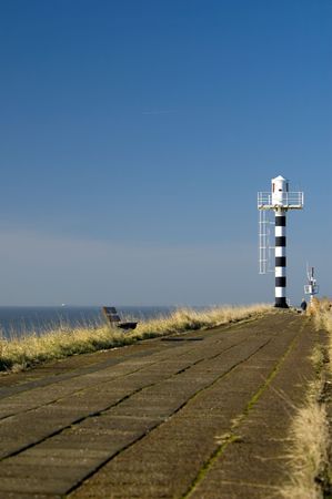 black and white lighthouse at the end of the road, against blue skyの写真素材