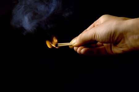 hand holding a burning match, isolated on black backgroundの写真素材