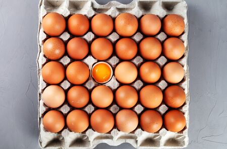 Chicken eggs in a paper tray, one egg is broken, gray background, top viewの写真素材