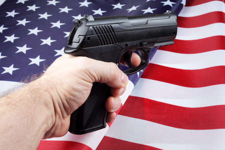 Pistol in a man's hand against the background of the American flag, selective focus.