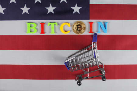 The inscription bitcoin and gold bitcoin on the flag of the United States, next to it is a cart from the supermarket, a place for your textの写真素材