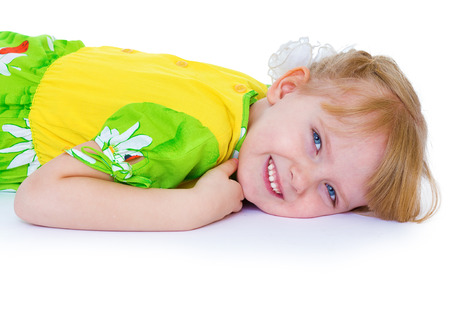 beautiful little girl in a green dress with daisies, lies in a chair on a white background and smilingの写真素材