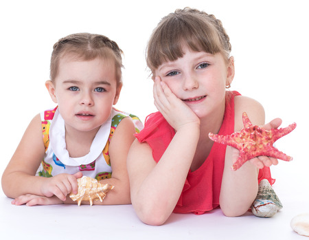 two little girls are playing and shells and starfish. Isolated on white background.の写真素材