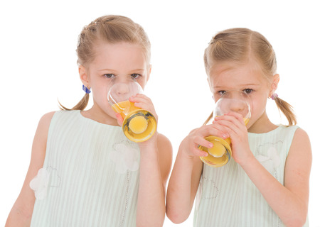  Cute sisters drink from a glass of fresh orange juice.Isolated on white .の写真素材