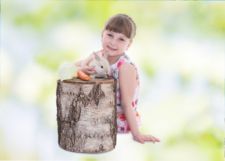 Smiling girl sitting near a tree stump with rabbit.の写真素材