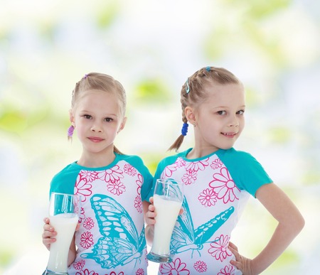 Charming twin sisters with glasses of milk kindergarten, the concept of childhood and joy, teensの写真素材