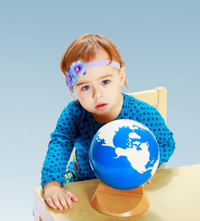 little girl examines the globe in the Montessori classroom on a blue background the concept of a happy childhood, education of children, teensの写真素材