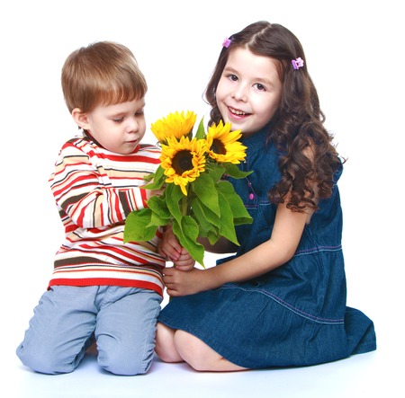 little brother with her older sister sitting on the floor and holding a bouquet of yellow flowers.Isolated on white background.の写真素材