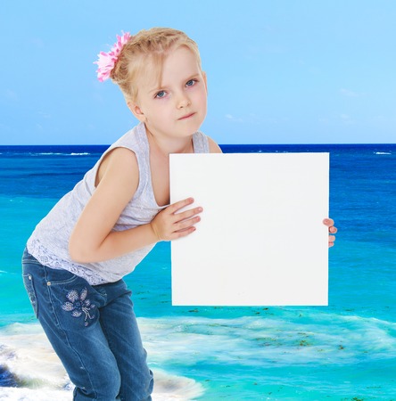 Girl in gray shirt holding a white banner on the background of the sea.の写真素材