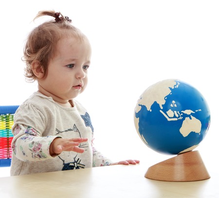 Little girl studying a globe sitting at the table.Isolated on white background.の写真素材