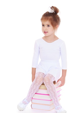 Adorable little girl is sitting on a big pile of books. Studio photo, isolated on white background.の写真素材