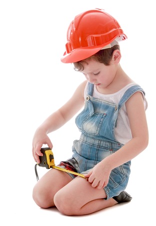 Funny little boy in denim overalls and a hard hat is considering building roulette-Isolated on white backgroundの写真素材