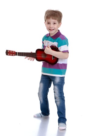 Cheerful little boy in jeans and a striped t-shirt strumming the guitar well, the boy is studying in a music school-Isolated on white backgroundの写真素材