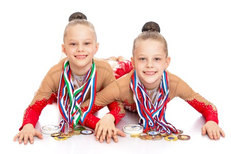 Two charming girls gymnasts in sports clothes lie on the floor and demonstrate the medals won at competitions. The medals hanging around their necks a lot of them.-Isolated on white backgroundの写真素材