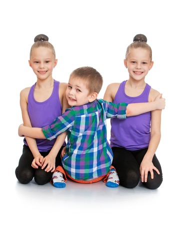two girls sisters in t-shirts and sports jerseys tights sat on his knees on the floor,hugging the boy's younger brother who sits in the chamber with his back turned his head , only three people-Isolated on white backgroundの写真素材