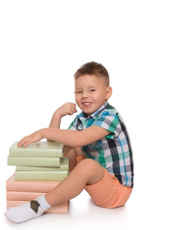 Smiling blond little boy sitting on the floor leaning on pile of books - Isolated on white backgroundの写真素材