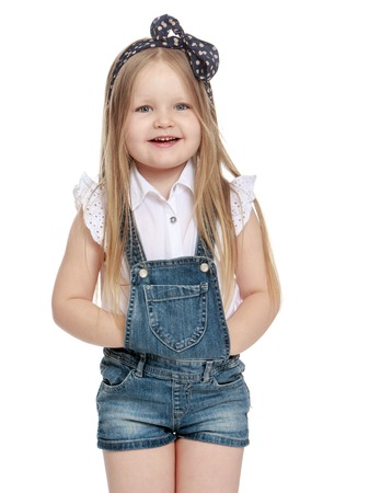 Adorable little blonde girl in short denim overalls with a bow on my head. Close-up - Isolated on white backgroundの写真素材