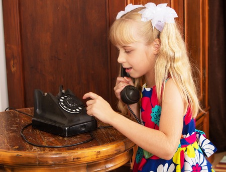 Adorable little blonde girl put your ear to the handset of the old phone. retro styleの写真素材