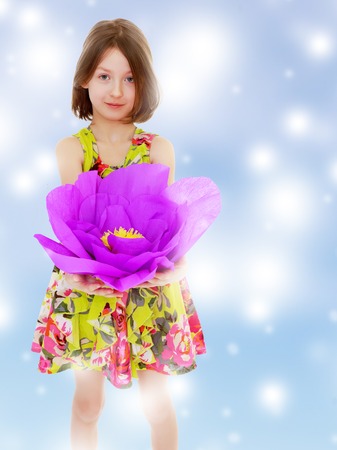 Adorable little girl in summer dress holding a large purple flower made of paper.Blue Christmas festive background with white snowflakes.の写真素材