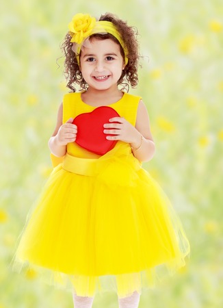 Adorable little girl in bright yellow elegant dress. Close to her heart.Bright,floral yellow-green blurred background.の写真素材