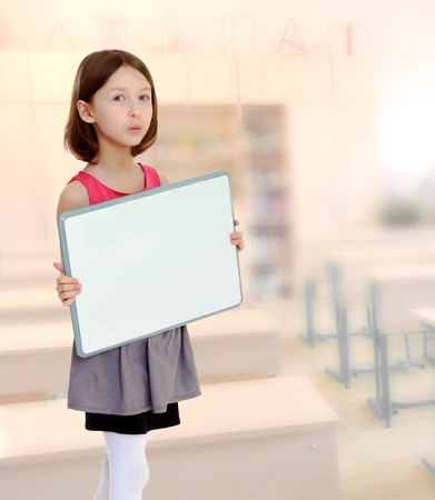 Beautiful, small, slender girl, holding in front of a white poster.During a lesson in school.の写真素材