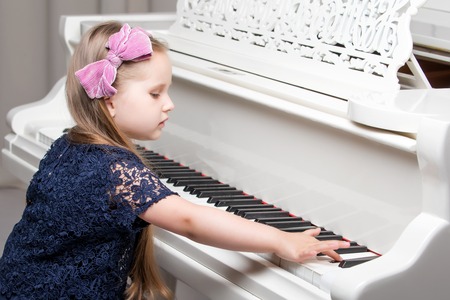 Beautiful little girl is playing on a white grand piano.の写真素材