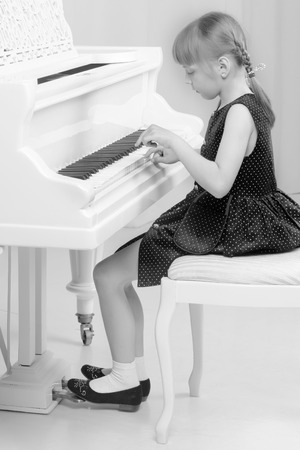 Beautiful little girl is playing on a white grand piano.の写真素材