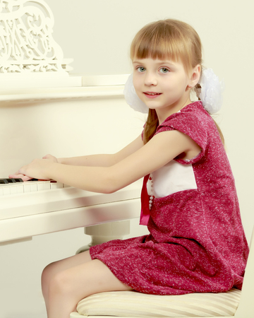 A little girl is sitting in front of a white grand piano.の写真素材