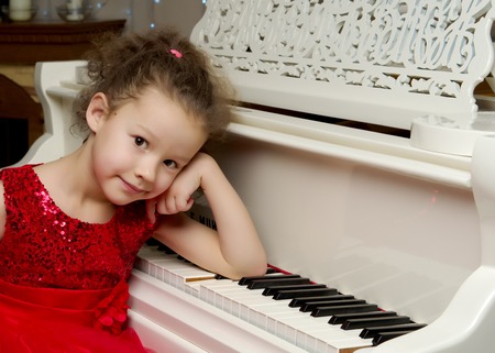 Beautiful little girl is playing on a white grand piano.の写真素材