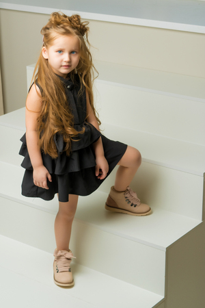 Beautiful little girl is sitting on the white staircase.の写真素材