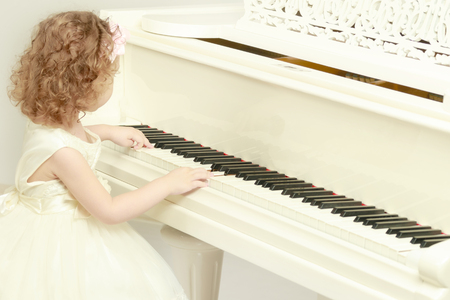 Beautiful little girl is playing on a white grand piano.の写真素材