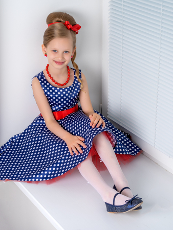 A little girl is sitting by the window with jalousieの写真素材