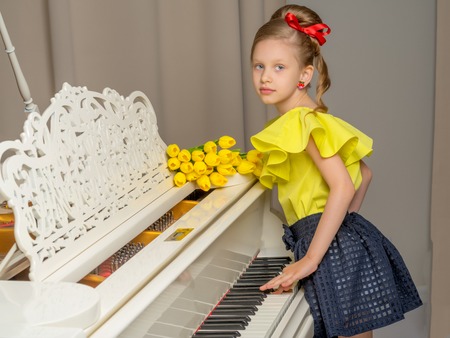 Girl schoolgirl near the piano on which lies a bouquet of flowerの写真素材