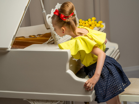 Girl schoolgirl near the piano on which lies a bouquet of flowerの写真素材