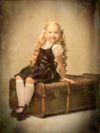 A little girl is sitting on an old suitcase.の写真素材