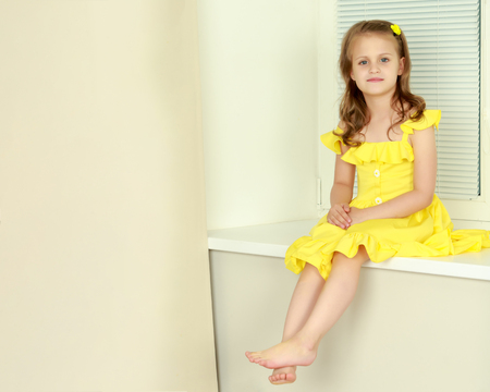 A little girl is sitting by the window with jalousieの写真素材