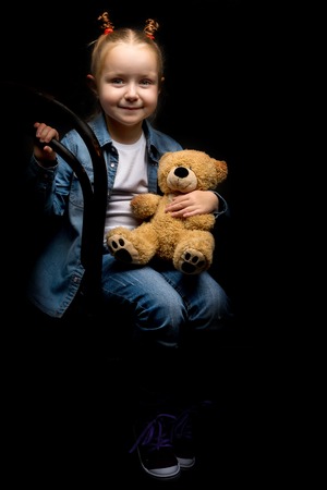 Little girl with a teddy bear on a black background.の写真素材