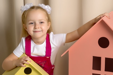 A little girl looks out from behind a toy wooden house.の写真素材