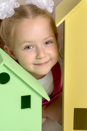 A little girl looks out from behind a toy wooden house.の写真素材
