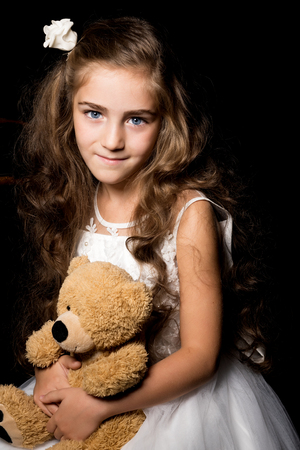 Little girl with a teddy bear on a black background.の写真素材