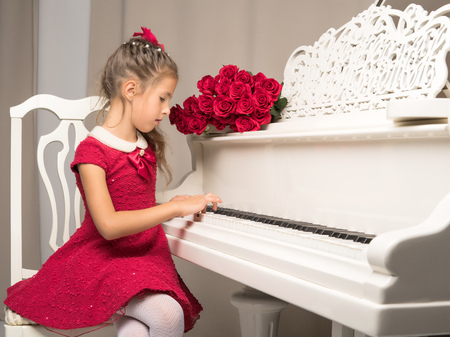 Girl schoolgirl near the piano on which lies a bouquet of flowerの写真素材