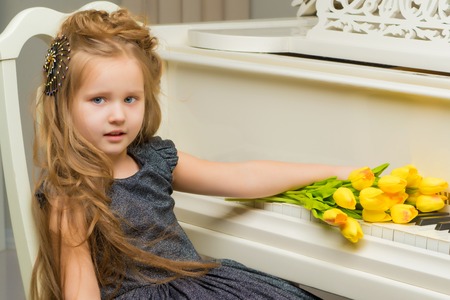 Girl near the piano on which lies a bouquet of flowers.の写真素材