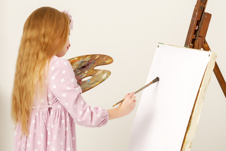 Little girl with a palette and brush near the easel.の写真素材